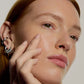 Close-up of a person's face with hand near the cheek, wearing multiple earrings.