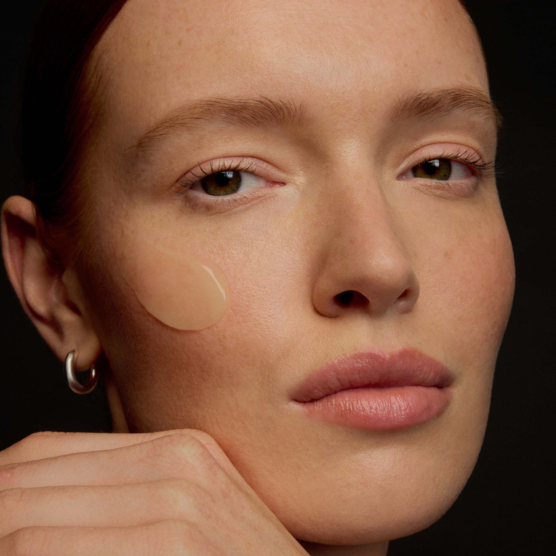 Close-up of a woman's face with concealer applied under her eyes on a dark background