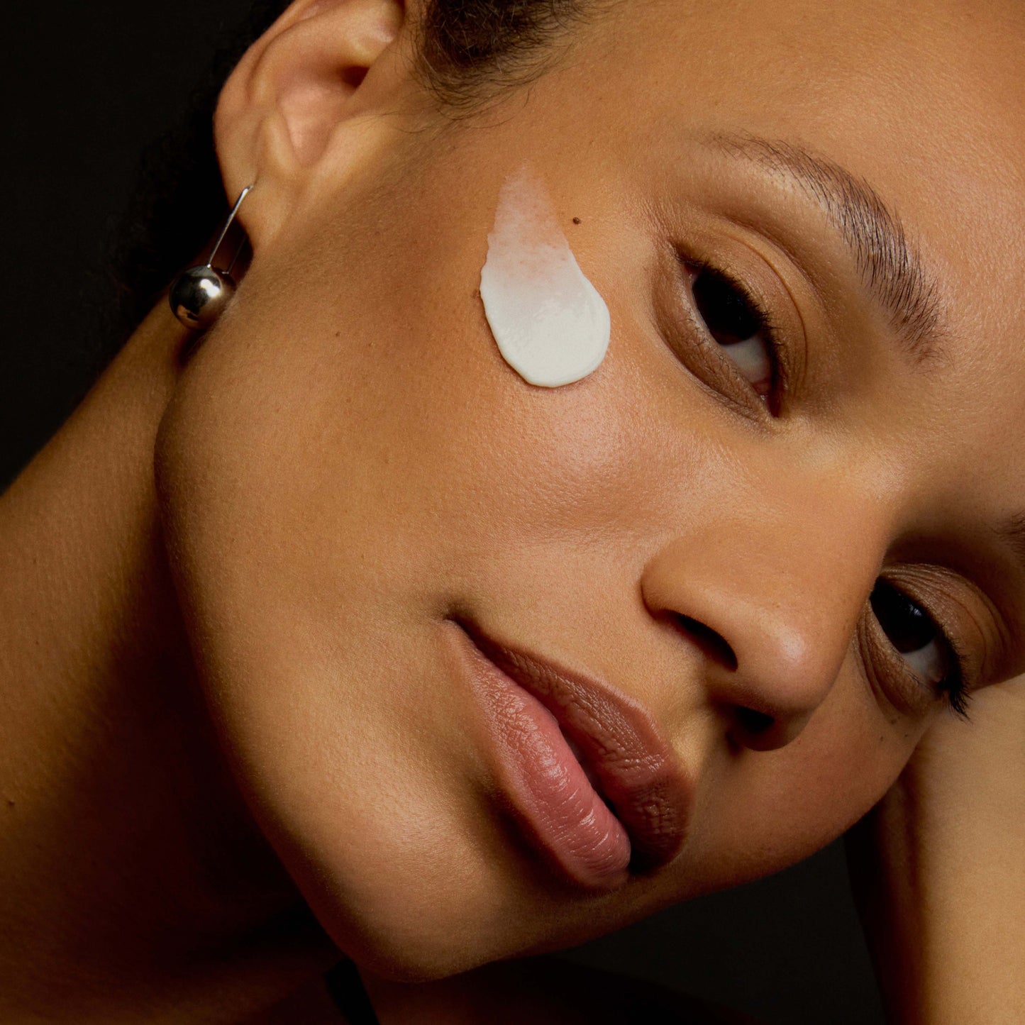 Close-up of a woman's face with a skincare product on her cheek against a dark background
